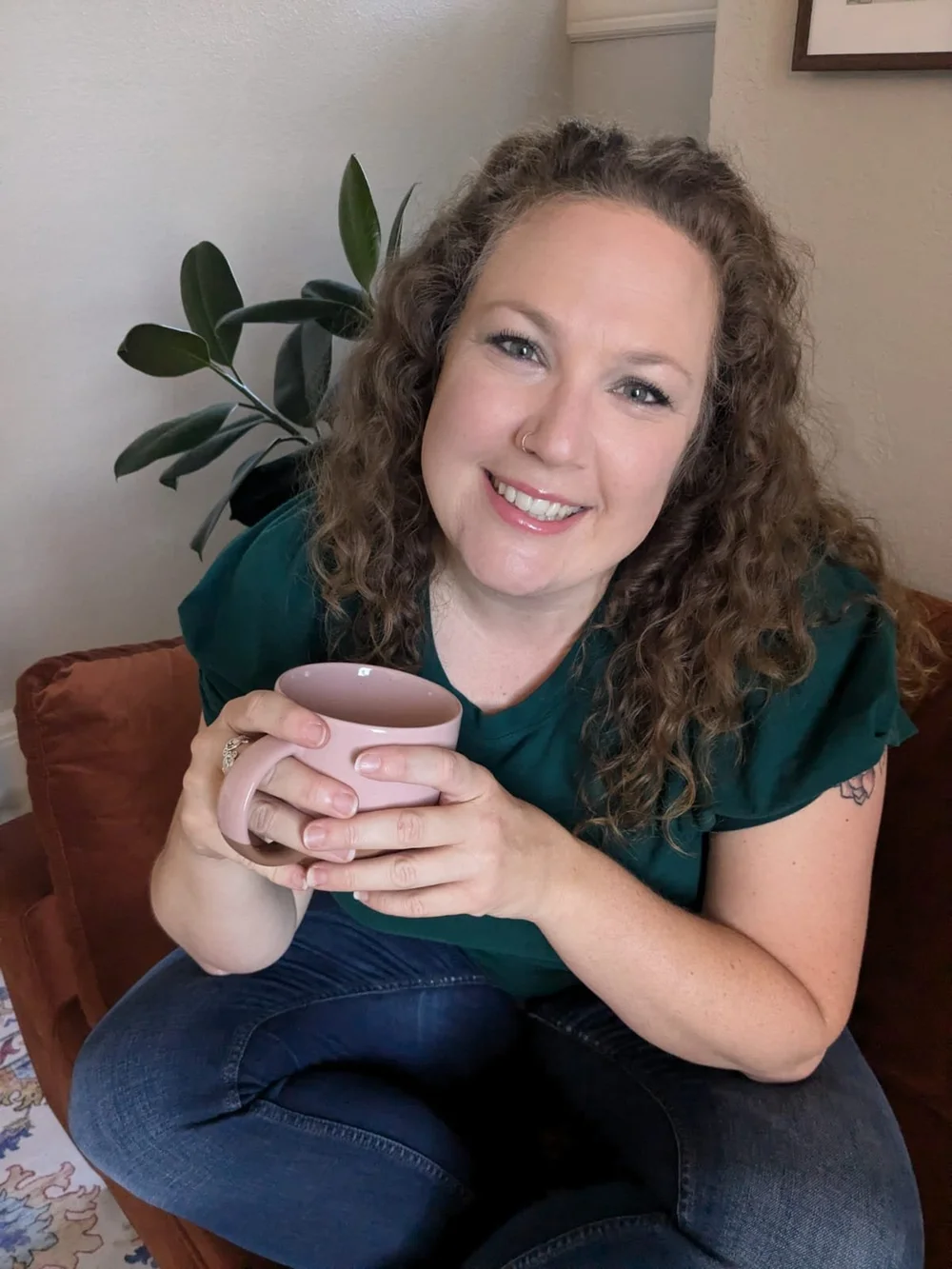 Katie smiling on a couch with a pink mug and a plant